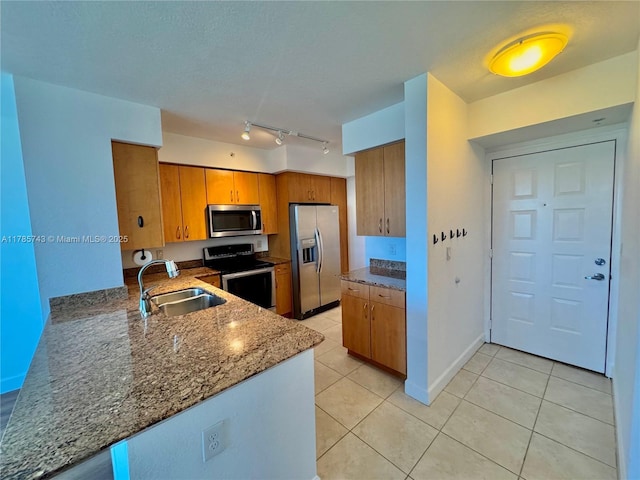 kitchen with stainless steel appliances, rail lighting, light tile patterned floors, a sink, and brown cabinetry