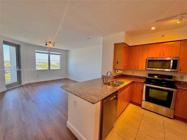kitchen with a sink, a textured ceiling, rail lighting, a peninsula, and appliances with stainless steel finishes