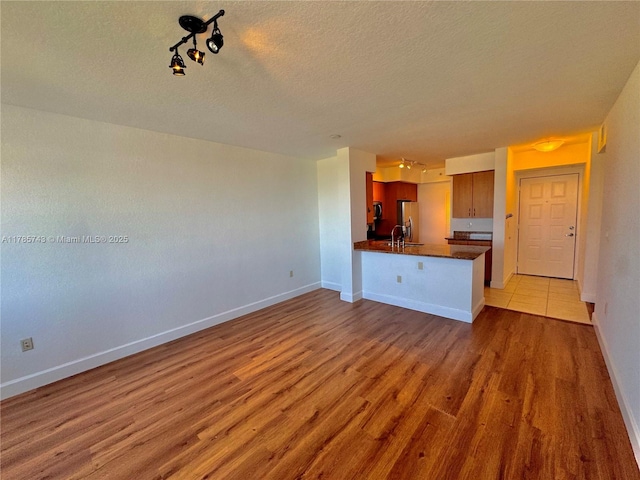 kitchen featuring dark countertops, a sink, wood finished floors, a textured ceiling, and freestanding refrigerator