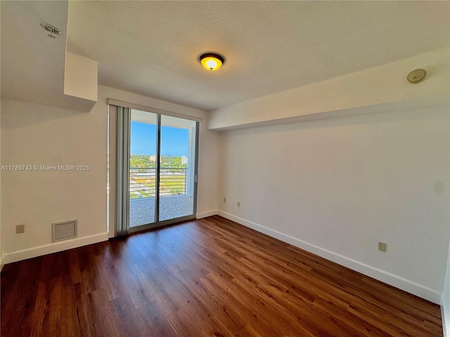 empty room featuring a textured ceiling, dark wood finished floors, visible vents, and baseboards