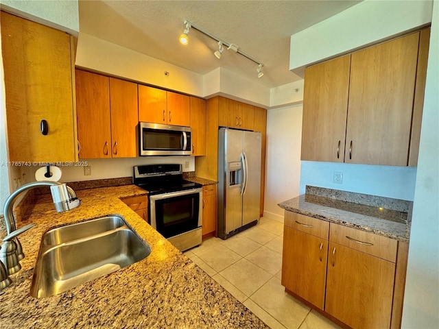 kitchen with stainless steel appliances, a sink, stone counters, track lighting, and light tile patterned floors