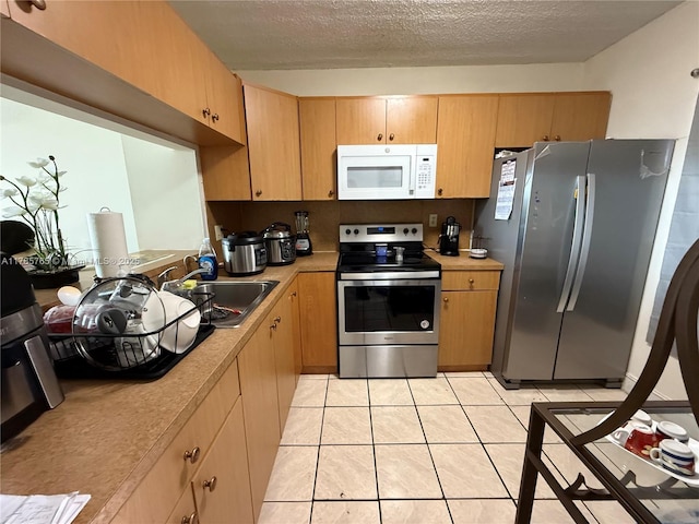 kitchen with light tile patterned floors, stainless steel appliances, light countertops, a sink, and a textured ceiling