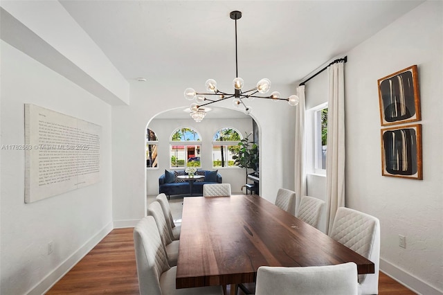dining space with arched walkways, wood finished floors, baseboards, and a notable chandelier