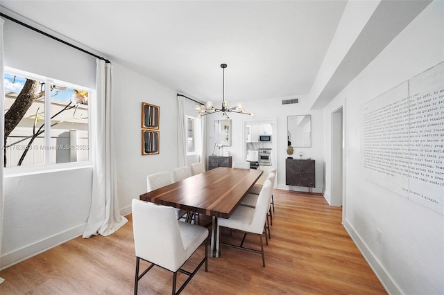 dining space featuring light wood-type flooring, visible vents, baseboards, and a notable chandelier