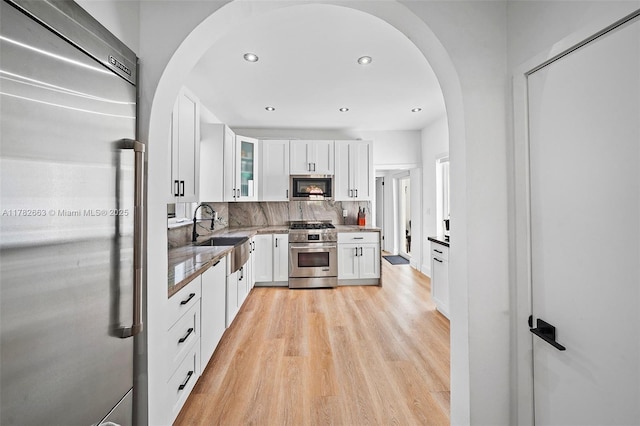 kitchen featuring light wood finished floors, arched walkways, a sink, white cabinetry, and high end appliances