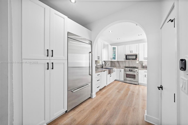 kitchen featuring light wood finished floors, a sink, backsplash, white cabinetry, and high end appliances