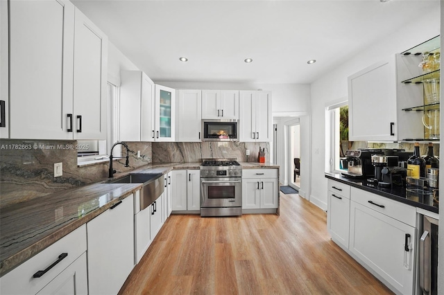 kitchen with white cabinets, a sink, light wood-style flooring, tasteful backsplash, and appliances with stainless steel finishes