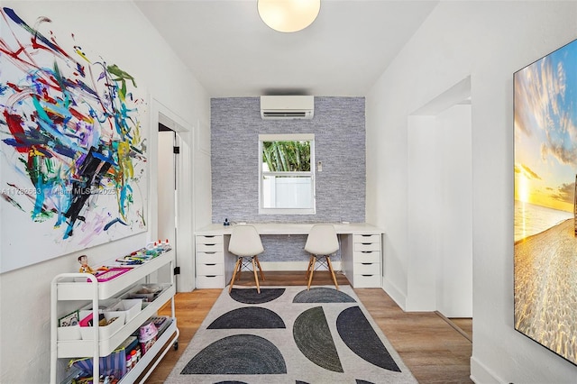 home office with built in study area, a wall mounted air conditioner, and wood finished floors