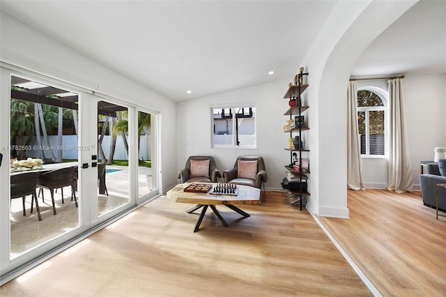 living area with french doors, arched walkways, vaulted ceiling, baseboards, and wood finished floors
