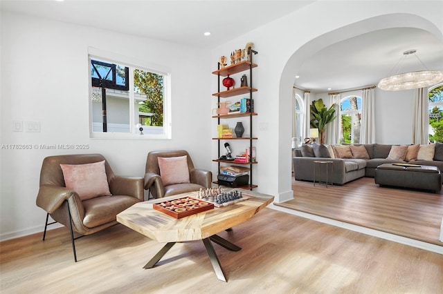 sitting room featuring a wealth of natural light, arched walkways, and light wood-style floors