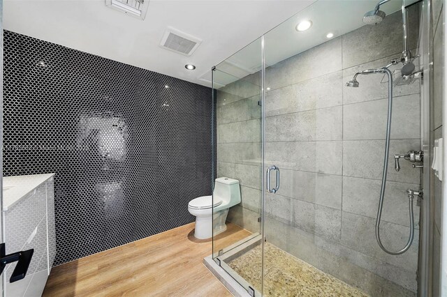bathroom with toilet, wood finished floors, visible vents, and a stall shower