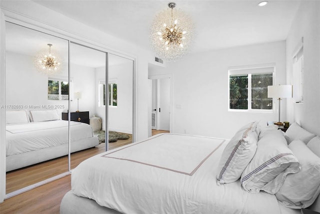bedroom with a closet, wood finished floors, visible vents, and an inviting chandelier