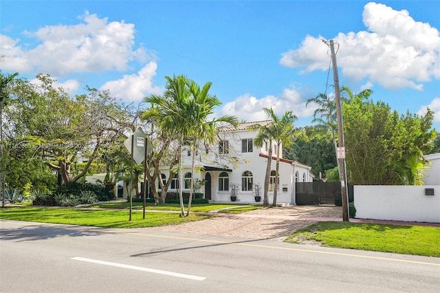 mediterranean / spanish-style home featuring stucco siding, fence, decorative driveway, and a front yard