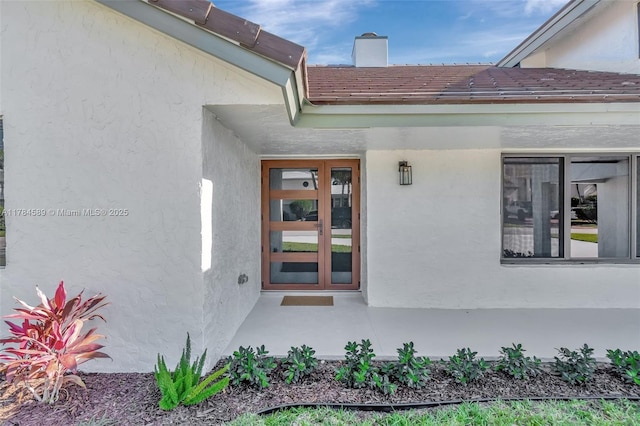 view of exterior entry featuring stucco siding and a chimney
