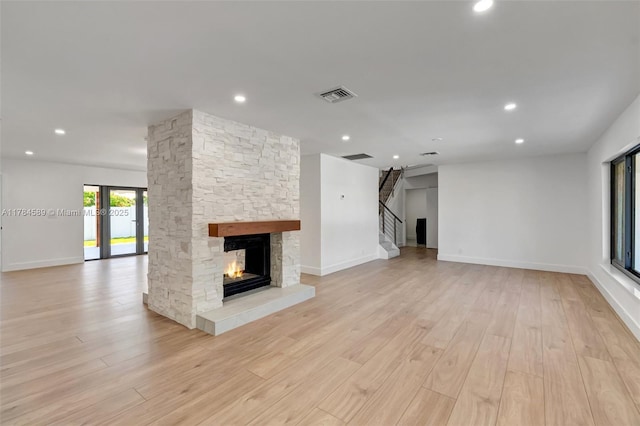 unfurnished living room with visible vents, a stone fireplace, light wood finished floors, and stairs