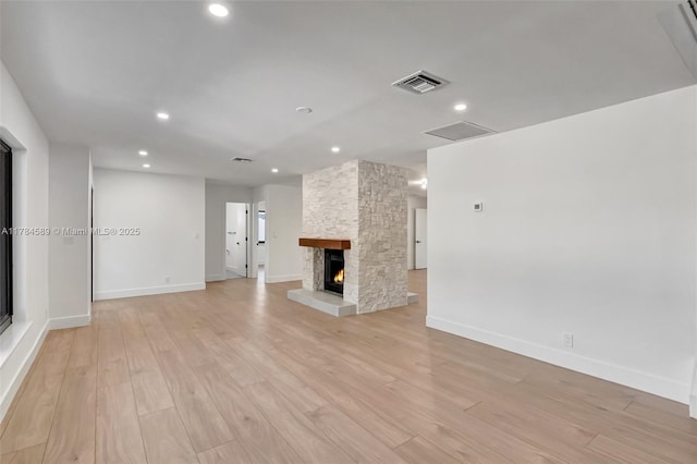 unfurnished living room with light wood-style flooring, visible vents, baseboards, and a stone fireplace