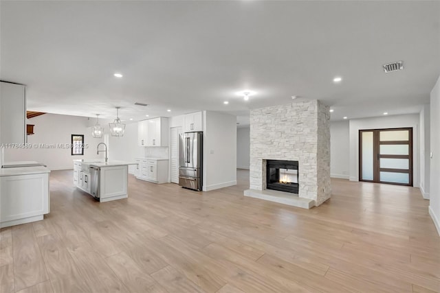 unfurnished living room featuring a sink, light wood-type flooring, baseboards, visible vents, and a fireplace