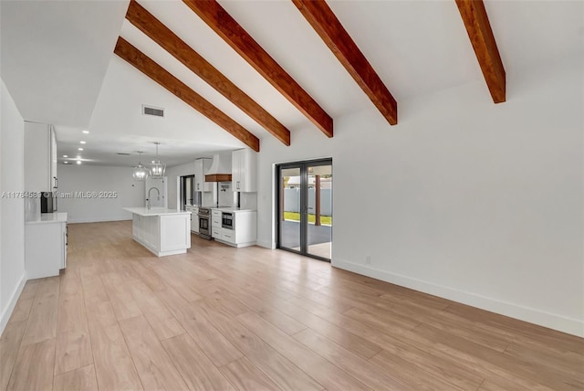 unfurnished living room with a sink, a chandelier, light wood-style flooring, baseboards, and visible vents