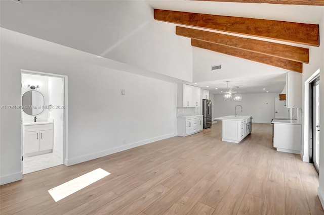 unfurnished living room featuring a sink, a chandelier, light wood-style floors, beam ceiling, and visible vents