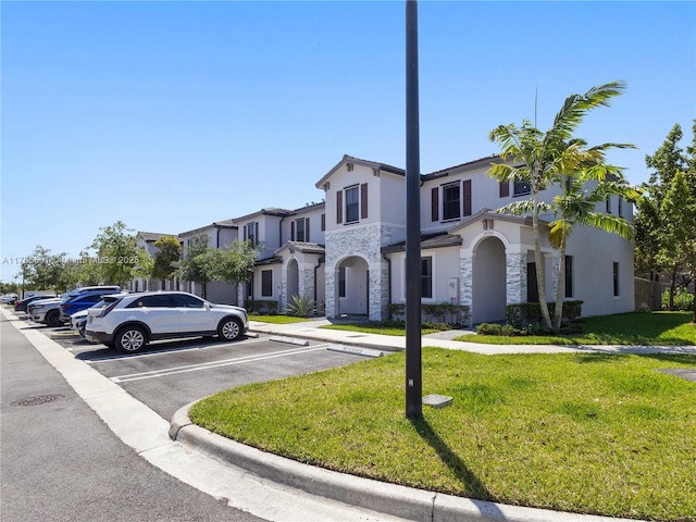 mediterranean / spanish-style home featuring uncovered parking, stone siding, a front yard, and stucco siding