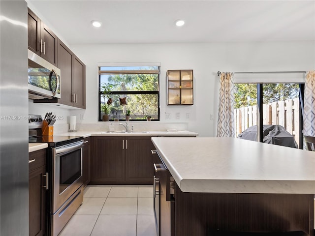 kitchen with a sink, light tile patterned floors, dark brown cabinetry, light countertops, and appliances with stainless steel finishes