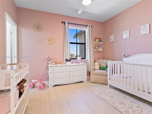 bedroom with ceiling fan, light wood-style floors, and a nursery area