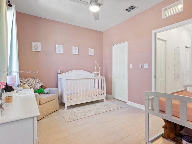 bedroom featuring a nursery area, light wood finished floors, electric panel, and visible vents