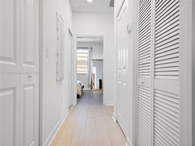 hall featuring baseboards, light wood-style flooring, and visible vents
