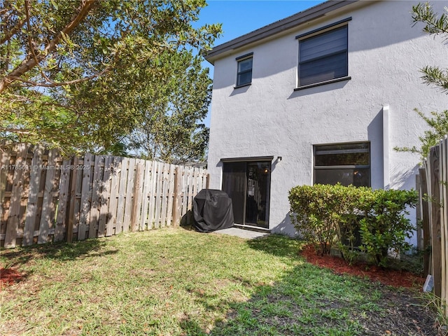 back of house featuring a lawn, a fenced backyard, and stucco siding