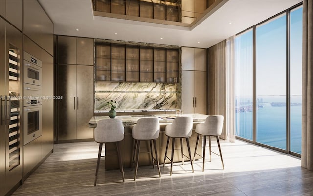 interior space featuring light wood-style flooring, bar area, a water view, recessed lighting, and a wall of windows