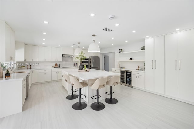 kitchen featuring stainless steel appliances, a sink, under cabinet range hood, a breakfast bar, and a center island