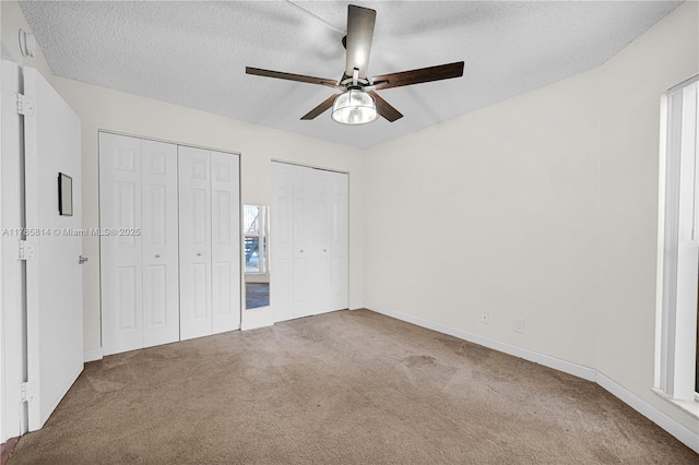 unfurnished bedroom with multiple closets, carpet floors, baseboards, a textured ceiling, and ceiling fan