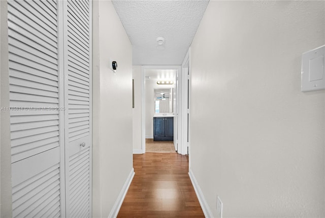 corridor featuring wood finished floors, a textured ceiling, and baseboards