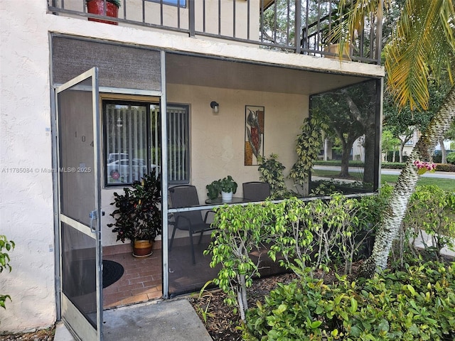 view of exterior entry featuring a balcony and stucco siding