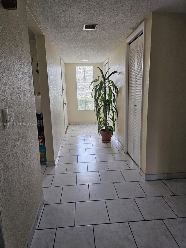 hallway featuring a textured wall, visible vents, a textured ceiling, and light tile patterned floors