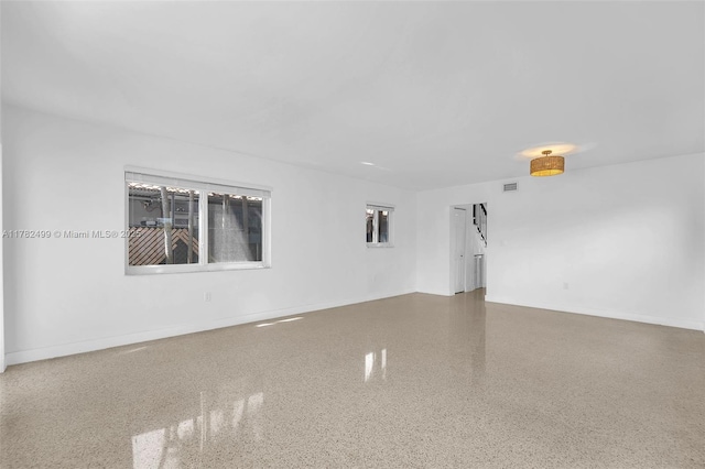 unfurnished room featuring baseboards, visible vents, and speckled floor
