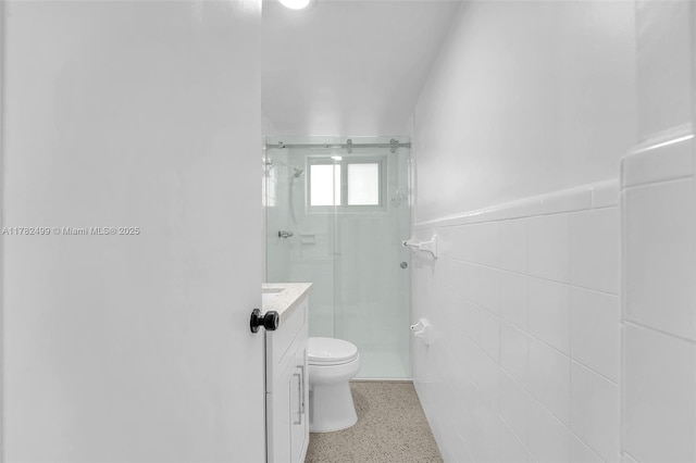 full bathroom with a wainscoted wall, toilet, tile walls, speckled floor, and a shower stall