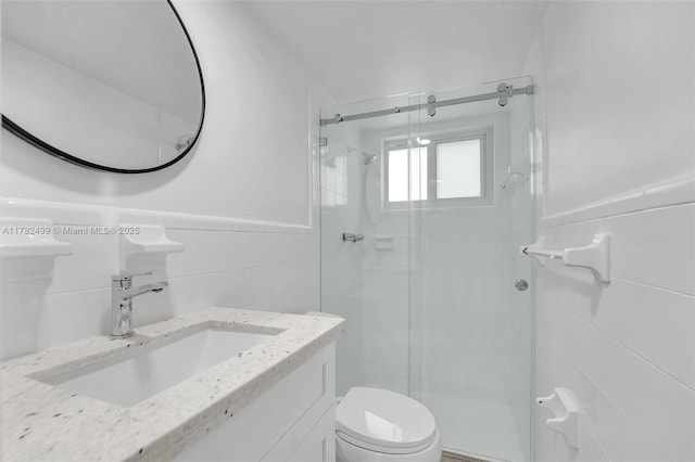 bathroom with toilet, a sink, tile walls, wainscoting, and a stall shower