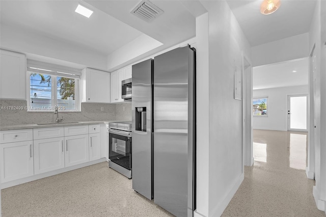 kitchen with white cabinets, stainless steel appliances, a sink, visible vents, and backsplash