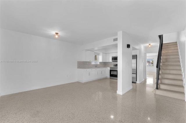 unfurnished living room with stairway, a sink, light speckled floor, baseboards, and visible vents