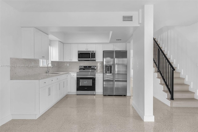 kitchen featuring stainless steel appliances, a sink, visible vents, baseboards, and decorative backsplash