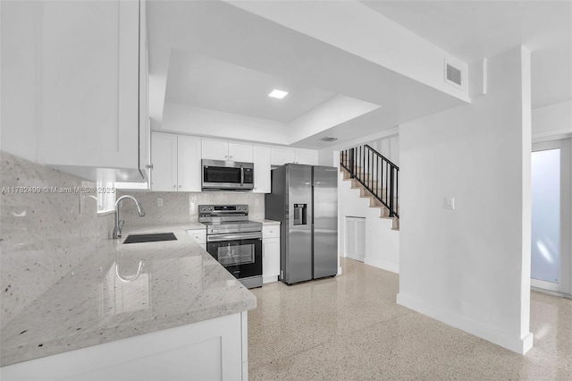 kitchen with a sink, visible vents, appliances with stainless steel finishes, light stone countertops, and a raised ceiling