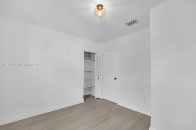 unfurnished bedroom featuring baseboards, wood finished floors, visible vents, and a closet