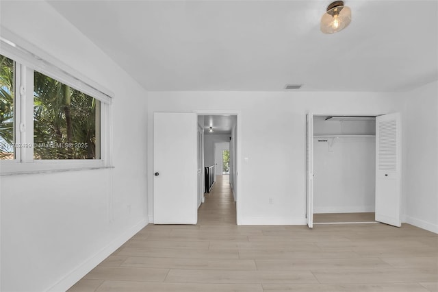 unfurnished bedroom with light wood finished floors, baseboards, visible vents, and a closet