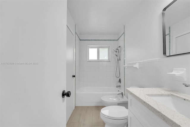 bathroom with washtub / shower combination, wood finished floors, toilet, vanity, and tile walls