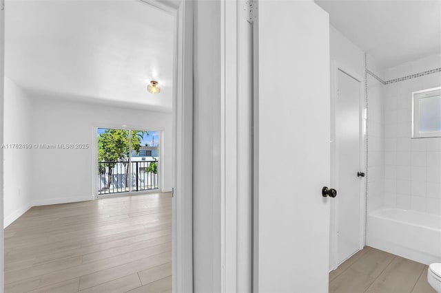 bathroom featuring toilet, washtub / shower combination, wood finished floors, and baseboards