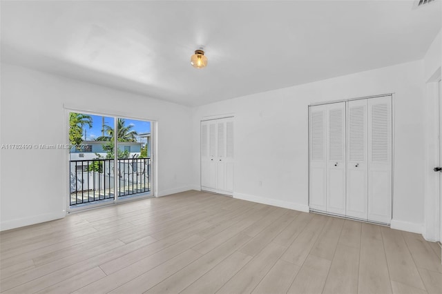 unfurnished bedroom with light wood-style floors, two closets, access to exterior, and baseboards