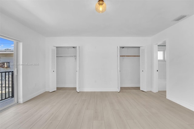 unfurnished bedroom with light wood finished floors, visible vents, two closets, and multiple windows