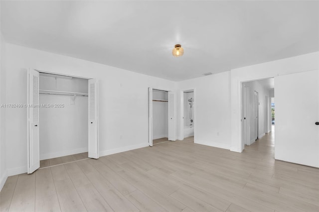 unfurnished bedroom featuring light wood finished floors, visible vents, and two closets