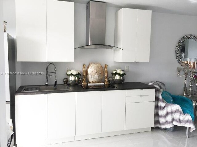 kitchen with dark countertops, a sink, white cabinets, wall chimney exhaust hood, and freestanding refrigerator